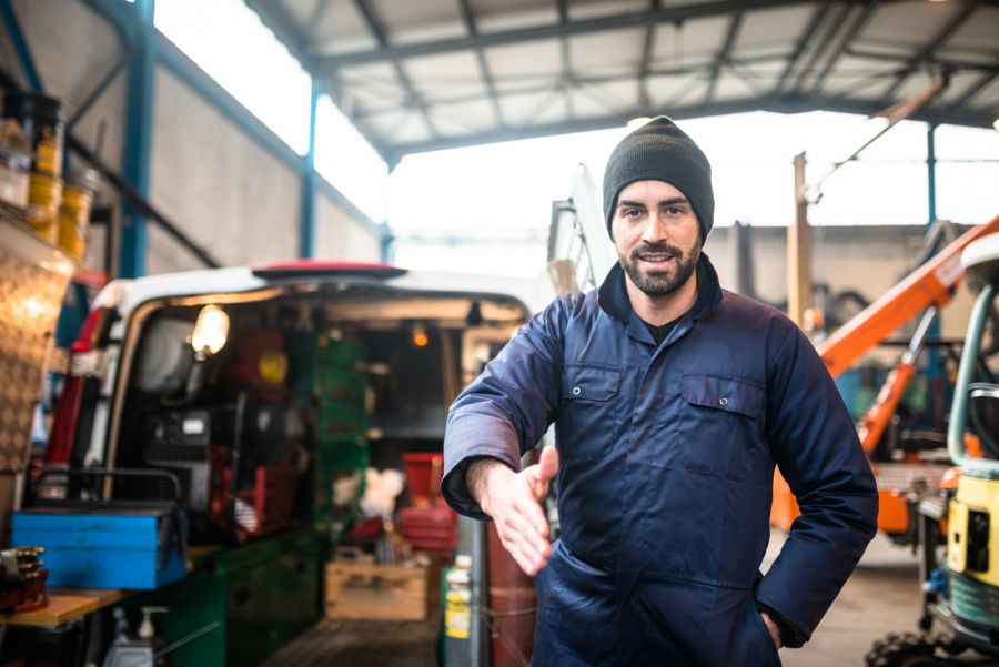 Mobile mechanic in workshop extending a hand for a handshake near service vans